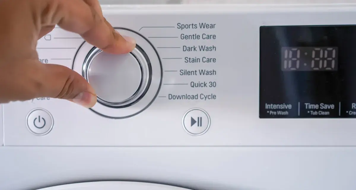 Mano che seleziona il programma risciacquo lavatrice. Opzioni: Sports Wear, Gentle Care, Dark Wash, Stain Care, Silent Wash, Quick 30, Download Cycle.