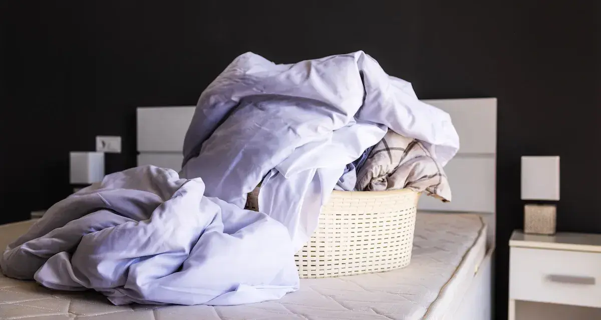Cesto di biancheria da letto accartocciata, pronto per il bucato. Un promemoria per imparare come smacchiare il lino e far brillare le lenzuola.