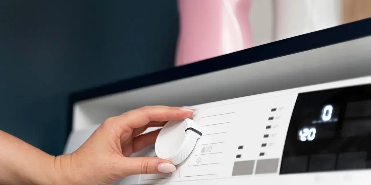Mano che gira la manopola della lavatrice per impostare la temperatura. A quanti gradi si lavano i colorati? Forse 30° o 40°.