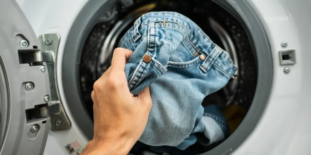 Mano inserisce jeans nella lavatrice. Scopri come lavare i jeans in lavatrice per mantenerli come nuovi.