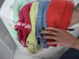 Mani che prendono un mucchio di lavatrice colorati: rosso, blu, giallo, rosa e verde menta.