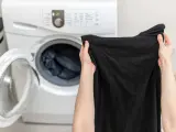 Mani che tengono capi neri, pronti per essere messi nella lavatrice aperta.