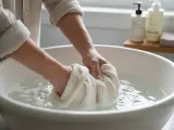 Mani che lavano delicatamente un maglione di cashmere in una bacinella, facendo attenzione che il cashmere si restringe se trattato male.