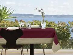 Tavola apparecchiata con tovaglia di lino bordeaux e beige, bicchieri, piatti e vaso con fiori. Un'idea su come rifinire una tovaglia di lino.