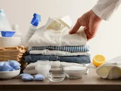 Mano indica una macchia su una camicia bianca, circondata da detersivi, bicarbonato per macchie di candeggina e limone.