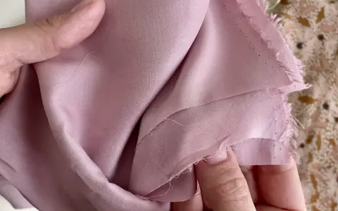 Mani che accarezzano un tessuto di viscosa rosa cipria, mostrando come lavare la viscosa a mano per preservarne la morbidezza.
