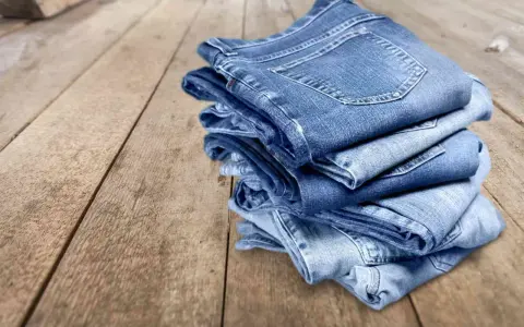 Pile di jeans su un tavolo di legno. Scopri come evitare che i jeans perdano colore.