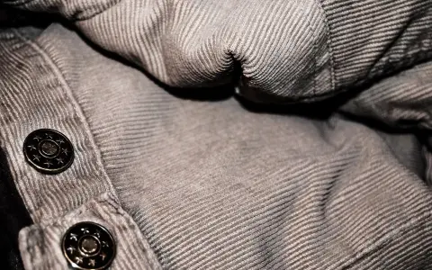 Dettaglio di un tessuto a coste marrone con bottoni metallici. Un invito a pulire le coste del tessuto per farle risaltare.