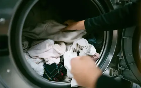 Mani che caricano la lavatrice con panni chiari, sperando di non trovare macchie bianche sui vestiti dopo lavatrice.