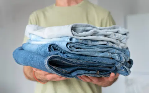 Un uomo tiene una pila di jeans duri dopo lavaggio, con tonalità di blu che vanno dal chiaro allo scuro.