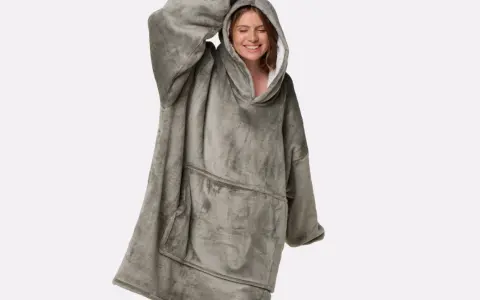 Donna sorridente indossa una coperta con cappuccio grigia, realizzata in poliestere, un materiale sintetico caldo e confortevole.