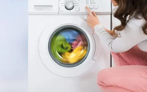 Donna preme il pulsante per avviare la lavatrice. Il cestello gira velocemente, mostrando i panni colorati in movimento.