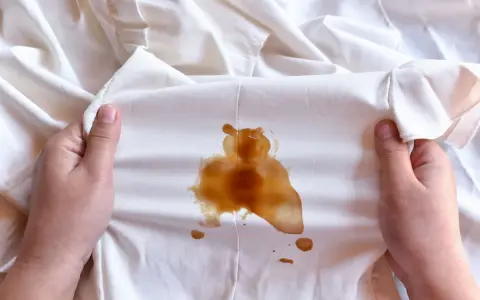 Mani che tengono un vestito bianco macchiato di caffè, forse caduto da una borsa in pelle.