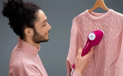 Uomo con maglione rosa usa un ferro da stiro verticale che non emette vapore, sperando di eliminare le pieghe.