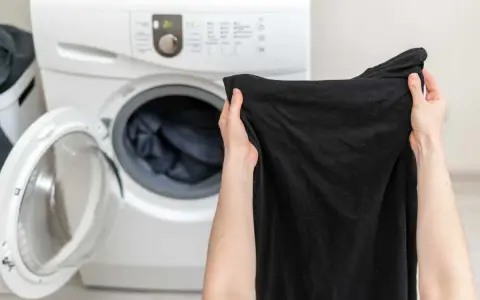 Mani che tengono capi neri, pronti per essere messi nella lavatrice aperta.
