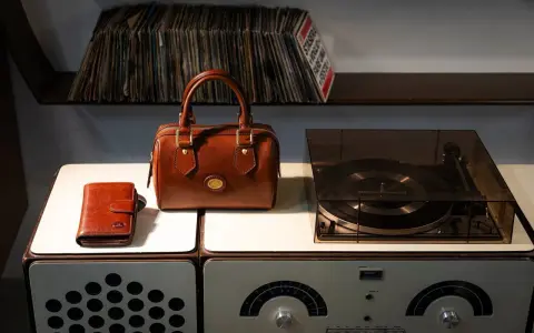 Borsa in pelle marrone, portafoglio e giradischi vintage. Un set per chi ama la musica e lo stile classico, pronto per essere pulito.