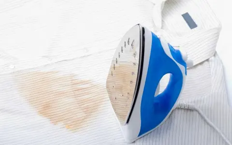 Un ferro da stiro blu e bianco lascia una macchia giallastra su una camicia bianca a righe sottili.