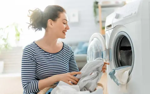 Donna sorridente carica la lavatrice con panni, inclusi tessuti sintetici.