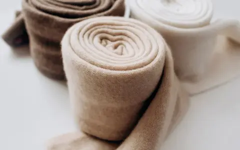 Rotoli di morbido cashmere in tonalità naturali, pronti per il lavaggio e la cura.