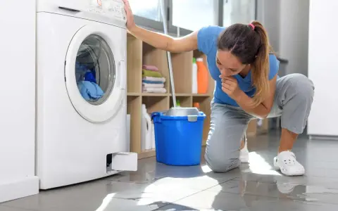 Donna preoccupata guarda la lavatrice che perde acqua e lascia residui di sporco sul pavimento.