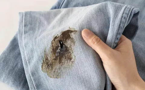 Mano che mostra un jeans macchiato, pronto per essere smacchiato.