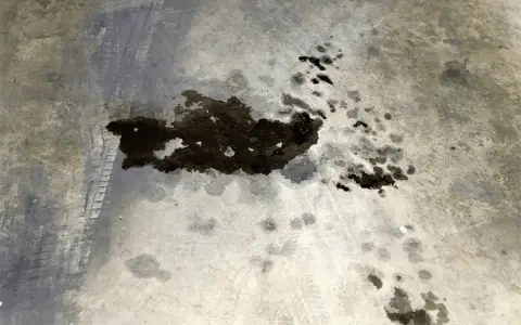 Macchie scure di grasso meccanico su cemento, con impronte di pneumatici. Un problema comune da risolvere per chi vuole togliere macchie di grasso meccanico.