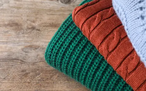 Close-up of folded knitted wool in green, rust, and light blue on a wooden surface.