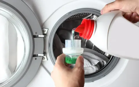 Versando detersivo liquido in un misurino per lavatrice. Ideale per capi delicati, cosa lavare a 20 gradi per preservare i colori.