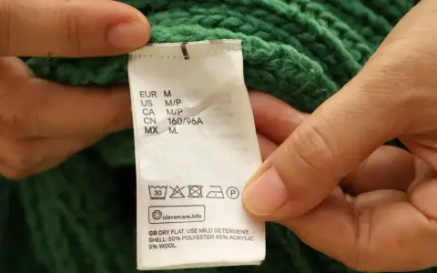 Etichetta di un maglione verde che indica il lavaggio in lavatrice a 30 gradi, con istruzioni per il lavaggio del cotone.