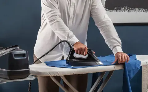 Uomo stira una camicia blu su un asse da stiro. Impara come stirare il poliestere con cura per risultati impeccabili.