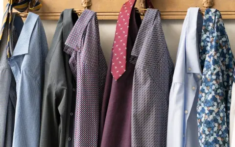 Camicie da uomo con fantasie diverse appese a un attaccapanni. Un promemoria su come lavare le camicie a mano per mantenerle perfette.