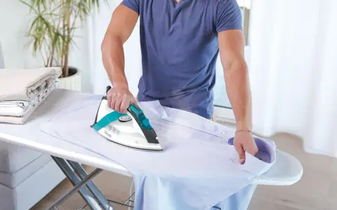 Uomo stira una camicia. Impara come pulire la piastra del ferro da stiro per risultati perfetti.