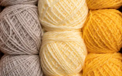 Gomitoli di lana in tonalità naturali: grigio, giallo tenue e giallo vivace. Diversi tipi di lana pronti per creare maglie calde.