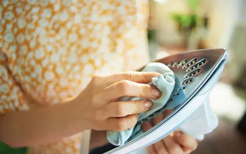 Mani che puliscono la piastra di un ferro da stiro con un panno, un metodo efficace per togliere la ruggine dal ferro da stiro e farlo tornare come nuovo.