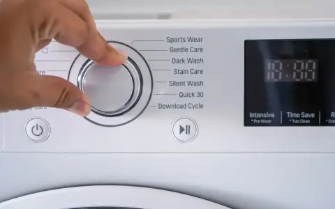 Mano che seleziona il programma risciacquo lavatrice. Opzioni: Sports Wear, Gentle Care, Dark Wash, Stain Care, Silent Wash, Quick 30, Download Cycle.
