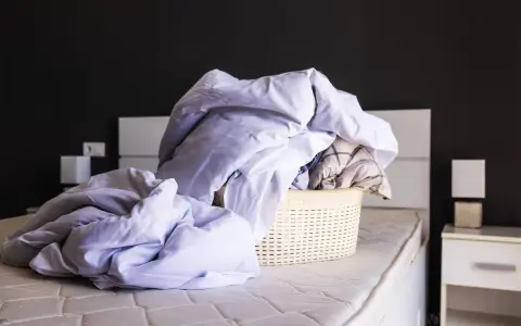 Cesto di biancheria da letto accartocciata, pronto per il bucato. Un promemoria per imparare come smacchiare il lino e far brillare le lenzuola.