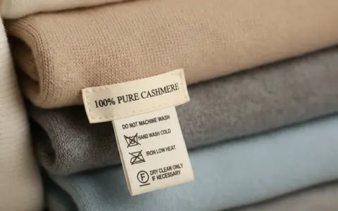 Pile di maglioni in cashmere. L'etichetta indica "100% PURE CASHMERE" e suggerisce il lavaggio a secco per preservare la morbidezza.