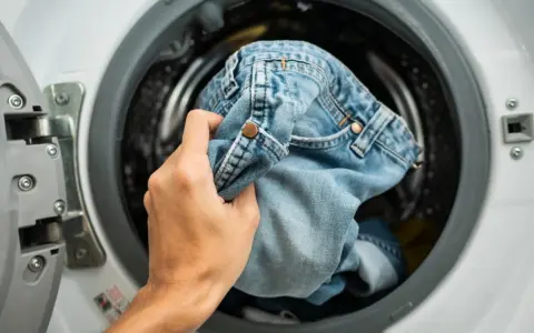 Mano inserisce jeans nella lavatrice. Scopri come lavare i jeans in lavatrice per mantenerli come nuovi.