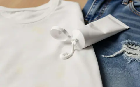 Tubo di crema sbiancante su maglietta bianca macchiata e jeans strappati. Scopri trucchi per togliere le macchie di candeggina.
