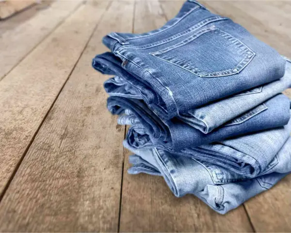 Pile di jeans su un tavolo di legno. Scopri come evitare che i jeans perdano colore.