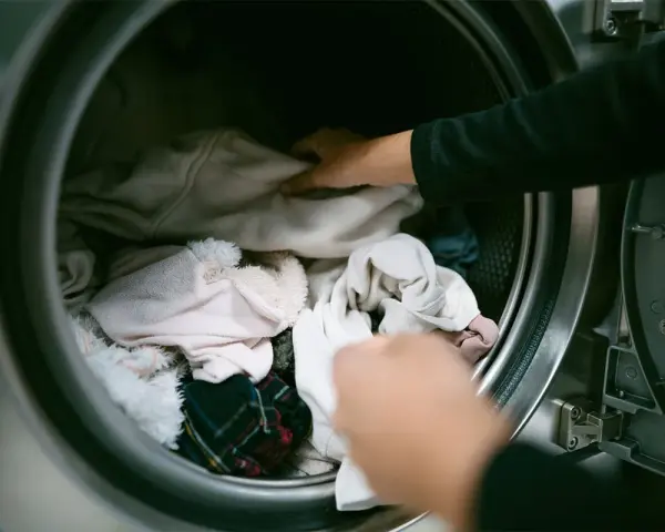 Mani che caricano la lavatrice con panni chiari, sperando di non trovare macchie bianche sui vestiti dopo lavatrice.