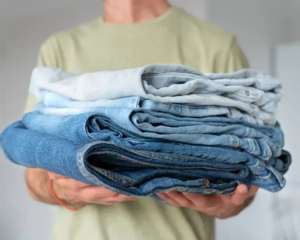 Un uomo tiene una pila di jeans duri dopo lavaggio, con tonalità di blu che vanno dal chiaro allo scuro.