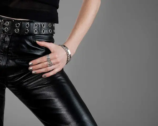 Dettaglio di persona con pantaloni di pelle nera, cintura con occhielli e gioielli. Guida su come lavare i pantaloni di pelle.