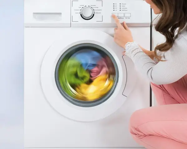 Donna preme il pulsante per avviare la lavatrice. Il cestello gira velocemente, mostrando i panni colorati in movimento.