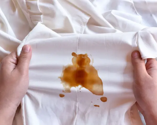 Mani che tengono un vestito bianco macchiato di caffè, forse caduto da una borsa in pelle.