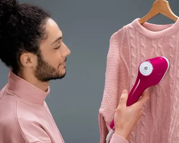 Uomo con maglione rosa usa un ferro da stiro verticale che non emette vapore, sperando di eliminare le pieghe.