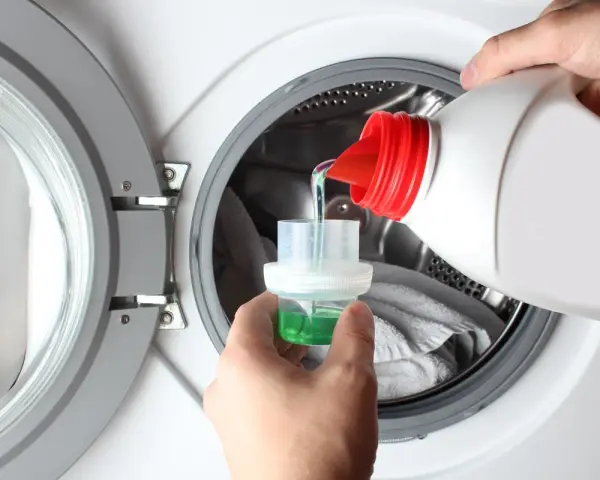Versando detersivo liquido in un misurino per il prelavaggio lavatrice.