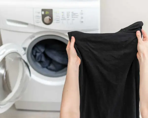 Mani che tengono capi neri, pronti per essere messi nella lavatrice aperta.