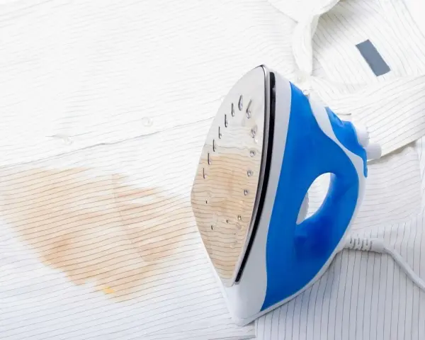 Un ferro da stiro blu e bianco lascia una macchia giallastra su una camicia bianca a righe sottili.