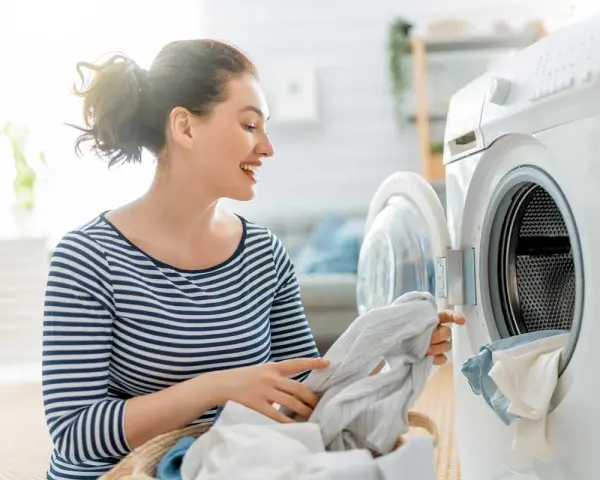 Donna sorridente carica la lavatrice con panni, inclusi tessuti sintetici.